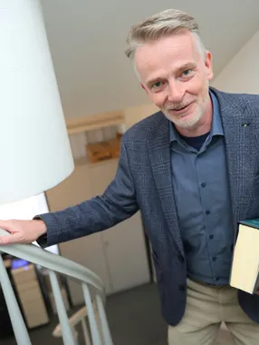 Ein Mann im dunkelblauen Sakko kommt mit einem Gesetzbuch in der Hand die Treppe herauf.