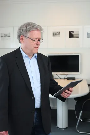 Ein Mann im schwarzen Sakko steht im Besprechungsraum und sieht auf ein Tablet.