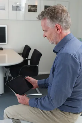 Ein Mann im blauen Hemd sitzt am Besprechungstisch und liest auf einem Tablet.