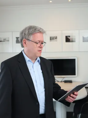 Ein Mann im schwarzen Sakko steht im Besprechungsraum und liest auf einem Tablet.