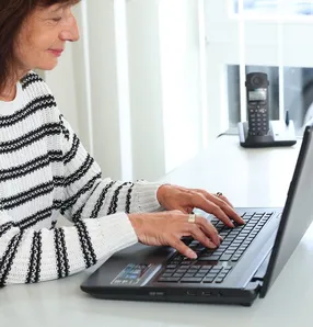 Eine Frau im gestreiften Pullover tippt auf einem Laptop.